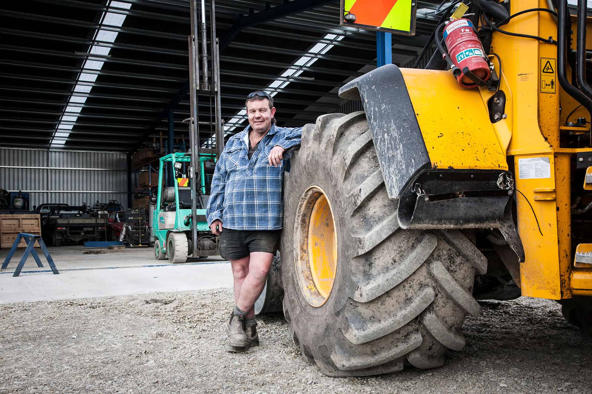 Staff photo, a man in a work shirt and safety boots beside a large agricultural machine